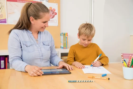 Frau und schreibendes Kind am Tisch sitzend
